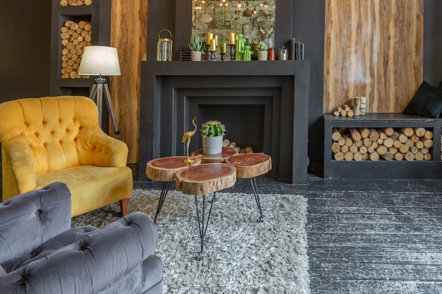 Dark brutal interior of sitting room decorated with wooden logs. yellow and grey soft armchairs, huge arc window and fireplace