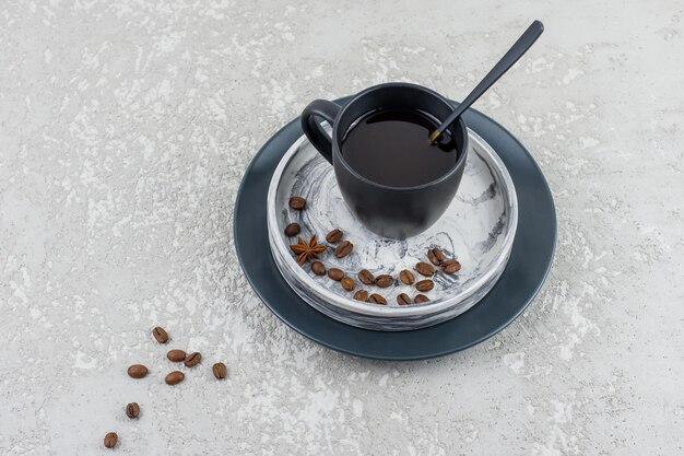 A dark ceramic cup with expresso on a plaster tray with coffee beans stands on a gray concrete table. top view. a copy of the space.