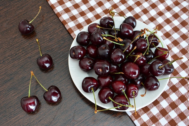 dark cherries on white plate on kitchen tablecloth isolated, close-up