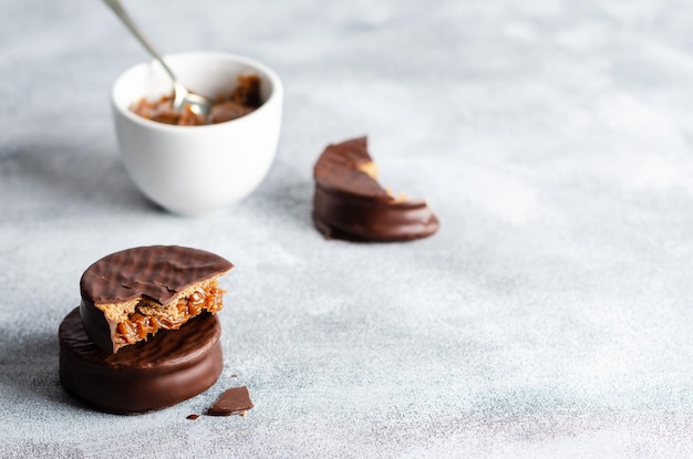 Dark chocolate alfajores and a bowl with dulce de leche, on grey background.