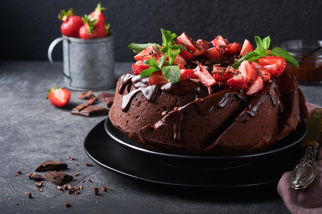 Dark chocolate bundt cake met ganache icing en aardbei op donkere stenen of betonnen tafelachtergrond feestelijke cake selectieve focus