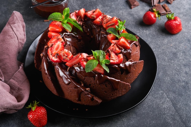 Dark Chocolate Bundt Cake with Ganache Icing and strawberry on dark stone or concrete table background Festive cake Selective focus