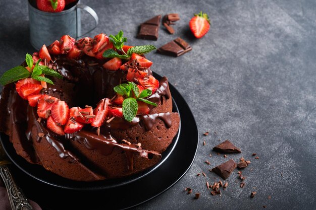 Dark Chocolate Bundt Cake with Ganache Icing and strawberry on dark stone or concrete table background Festive cake Selective focus