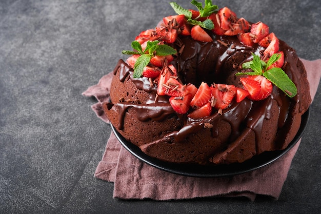 Dark chocolate bundt cake with ganache icing and strawberry on\
dark stone or concrete table background festive cake selective\
focus