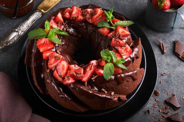 Torta bundt al cioccolato fondente con glassa di ganache e fragola su pietra scura o sfondo del tavolo in cemento torta festiva messa a fuoco selettiva