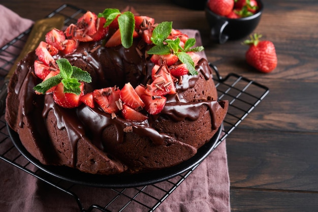 Photo dark chocolate bundt cake with ganache icing and strawberry on dark stone or concrete table background festive cake selective focus