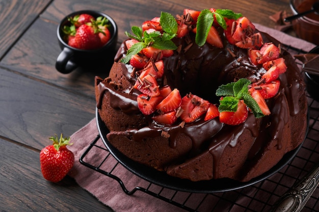 Photo dark chocolate bundt cake with ganache icing and strawberry on dark stone or concrete table background festive cake selective focus