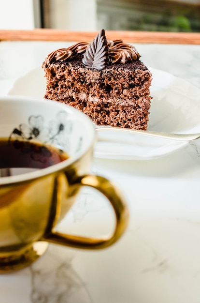 Dark Chocolate cake on a white plate and yellow gold cup of tea. Selective focus. Sweet birthdaydessert. Seasonal and holidays concept