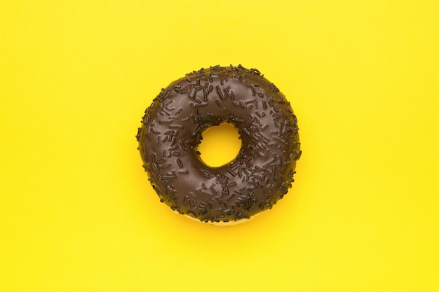 Фото Пончик из темного шоколада на ярко-желтом фоне минимальная концепция популярной выпечки