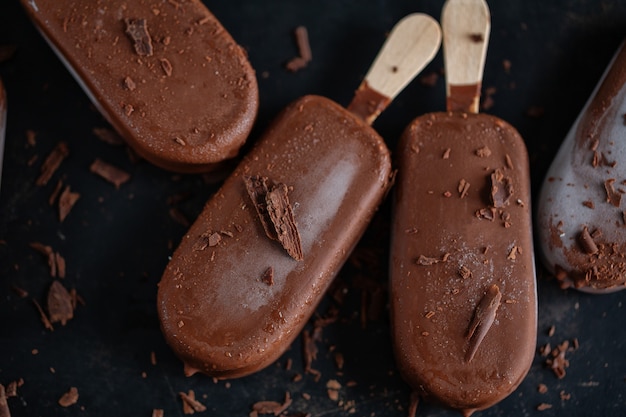 Dark chocolate ice cream popsicles with grated chocolate on dark plate. Closeup