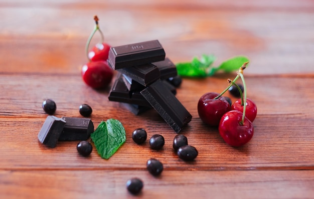 Dark chocolate in pieces isolated on wooden table with red cherries