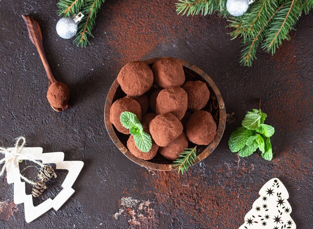 Dark chocolate truffles with raw cocoa powder, mint and fir tree branches. Christmas composition.