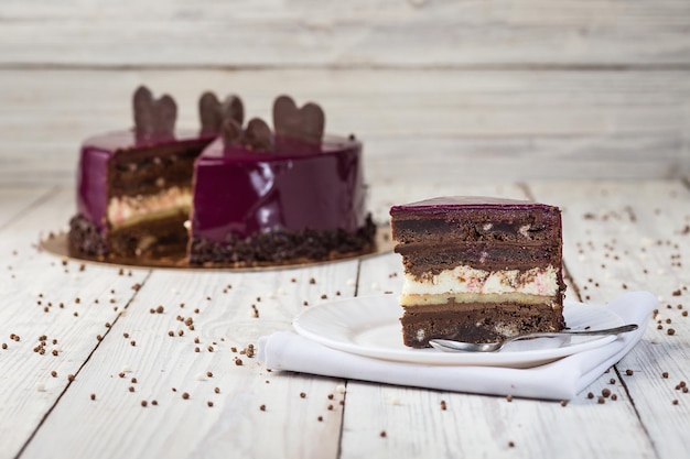 Dark chocolate vegan cake with cream and fruit mirror glaze on
wooden background