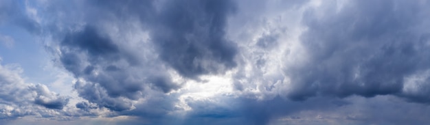 Dark clouds against a blue sky with sunbeams shining through. Sky panorama.