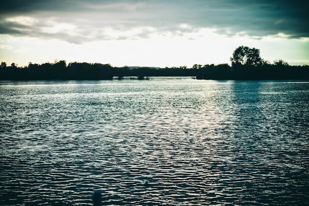 Dark clouds at sunset, sunrise above the water surface, filter