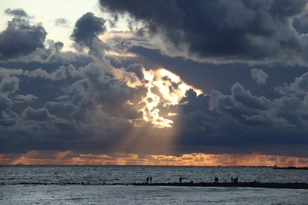 写真 海岸の人々の黒いシルエットの海に沈む夕日を背景に光線と暗い雲