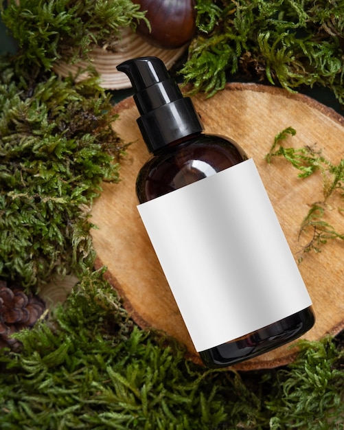 Dark Cosmetic bottle with blank label on wooden piece between green moss top view mockup