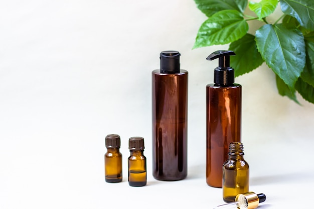 Dark cosmetic bottles and green natural leaves on a light background