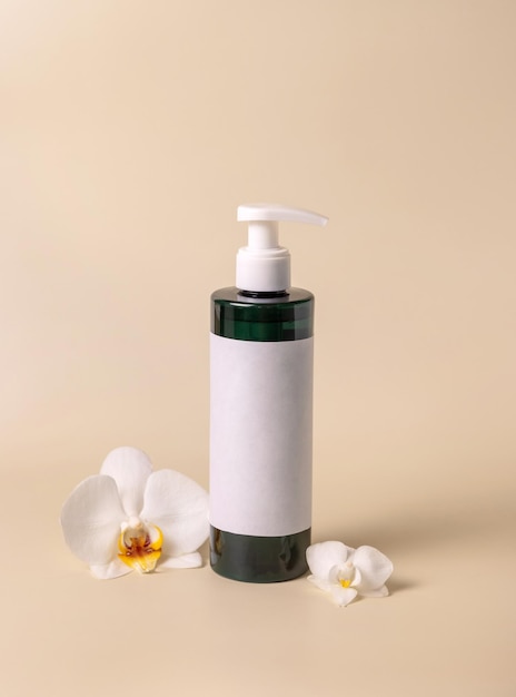 Bottiglia cosmetica scura con una pompa con etichetta vuota vicino a fiori di orchidea bianchi mockup