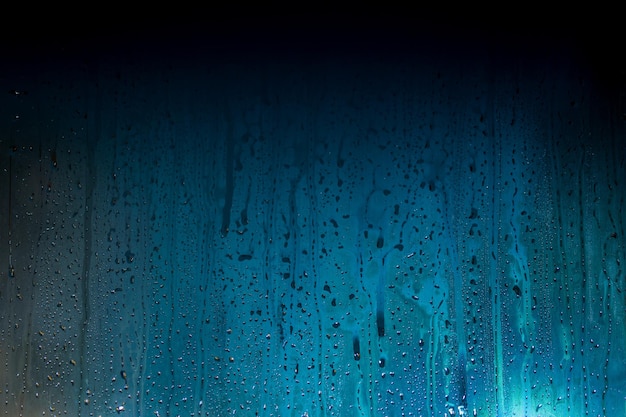 Dark cyanblue to black gradient background of night wet glass with water drops and smudges