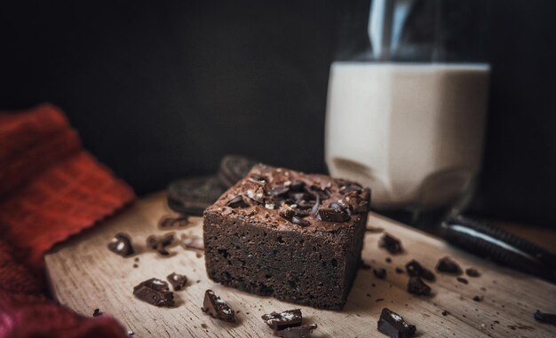 Photo dark fudge brownie on the wooden plate decorates with chocolate flakes and a glass of milk