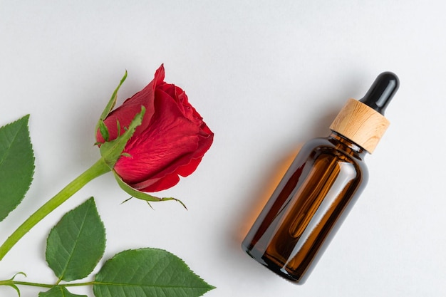 Dark glass bottle of cosmetic liquid and rose flower dropper\
bottle hyaluronic acid oil serum skin care product top view\
mockup