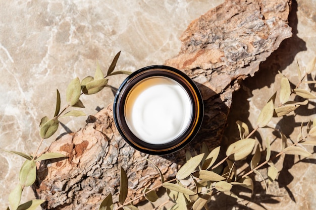 Photo dark glass jar with cream with peptides branch of dried eugalyptus on marble table herbal aromatherapy and skincare