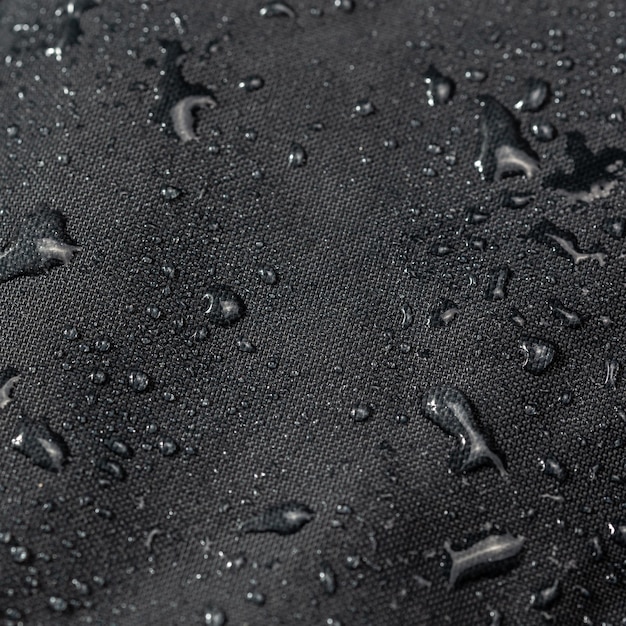 Dark gray waterproof hydrophobic cloth closeup with water drops selective focus background