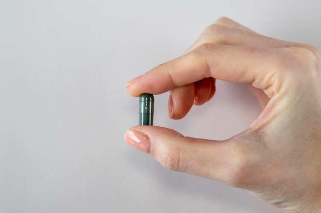 dark green capsule with chlorophyll or spirulina in a woman's hand helpful supplements or medicines on a beige background