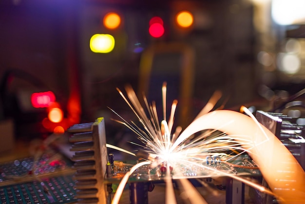 A dark green electronic printed circuit chip for TFT with bright multicolored wires lies on the wooden table of a talented engineer and sparkles with bright electric sparks of current