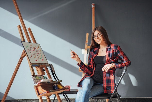 Dark-haired artist holding a brush in his hand and draws a picture on canvas.