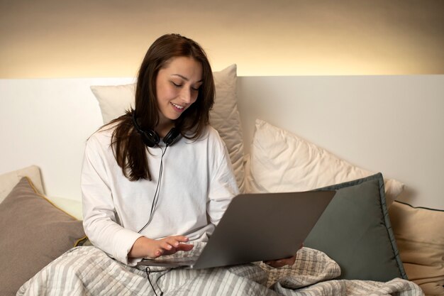 Dark-haired girl sitting in bed with smile looking at laptop and sending message