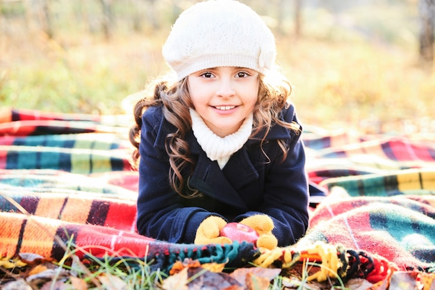 Темноволосая девушка улыбается лежа на одеяле в парке осенью. Фото высокого качества