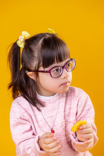 Dark-haired girl with down syndrome carrying orange chips in her hand