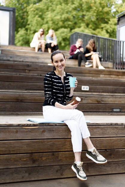 彼女の手にアイスクリームと青いガラスのコーヒーを持つ黒髪の少女は、夏の公園、レジャーコンセプトのベンチに座っています