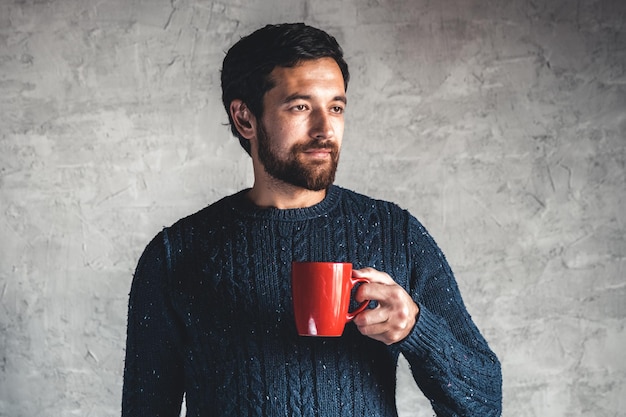 Foto il ragazzo dai capelli scuri tiene una tazza rossa in mano su uno sfondo grigio