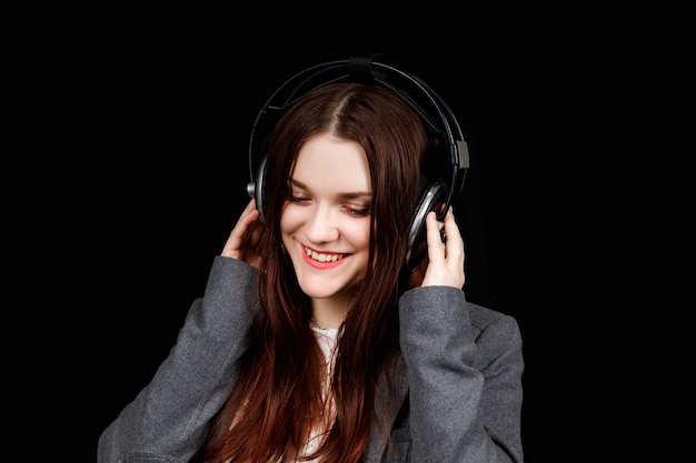 Dark haired model is posing in a dark studio with a headphones on her head