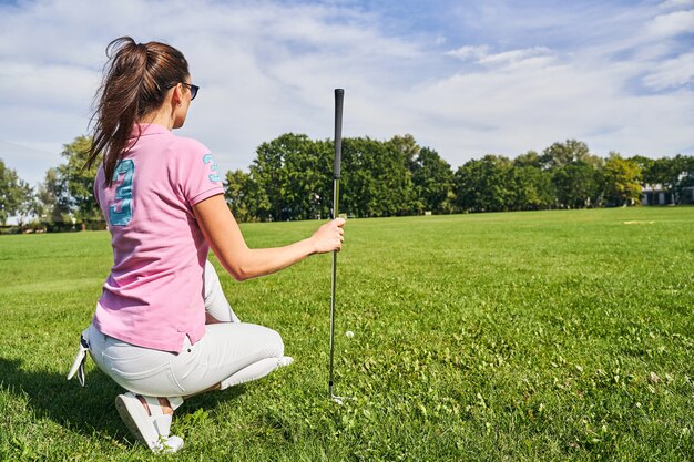 dark-haired woman in sunglasses checking the ground on the driving range