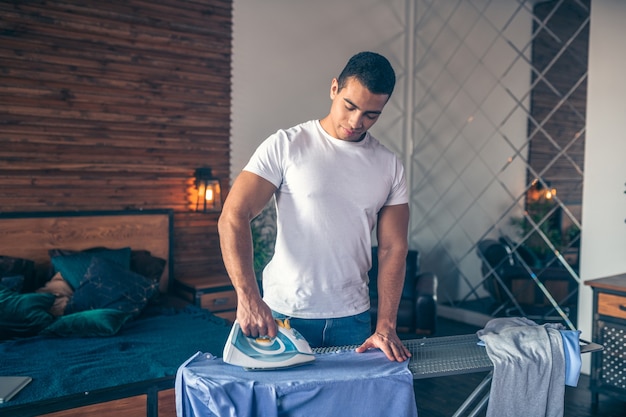 彼の手に鉄を持って立っている白いTシャツの黒髪の若い男