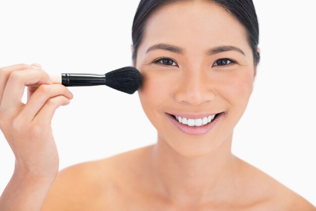 Dark haired young model applying powder on her face