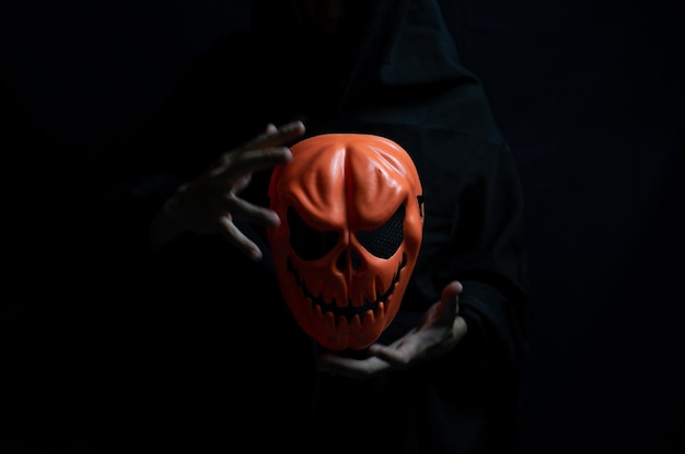 Dark Halloween Concept Orange ghost mask in hands of devil