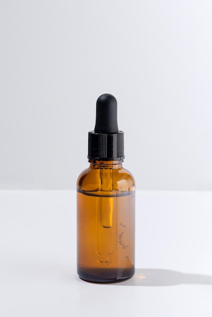 Dark jar of serum on white isolated background Mockup of container with dropper lid with collagen in rays of hard sunlight