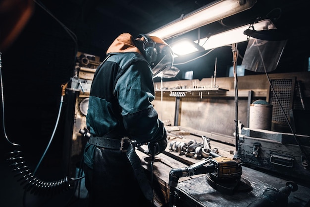 In the dark metal factory busy man is working on his workplace.