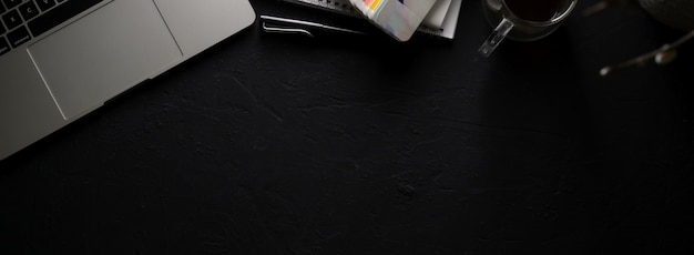 Фото Темное современное рабочее пространство с ноутбуком, канцелярскими принадлежностями, расходными материалами, чашкой кофе на черном столе