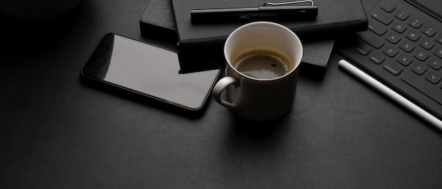Dark modern workspace with tablet keyboard, smartphone, coffee cup, schedule books and copy space