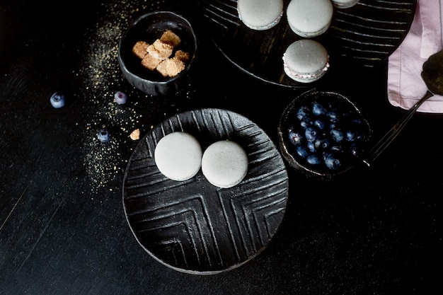 Dark monochrome photography Grey cakes macaroons on the dark surface of the table next to a spoon and sugar bowl with brown sugarAnd pink towels of plain cloth