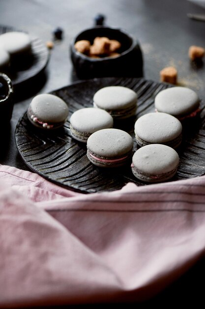 Dark monochrome photographyGrey cakes macaroons on the dark surface of the table next to a spoon and sugar bowl with brown sugar