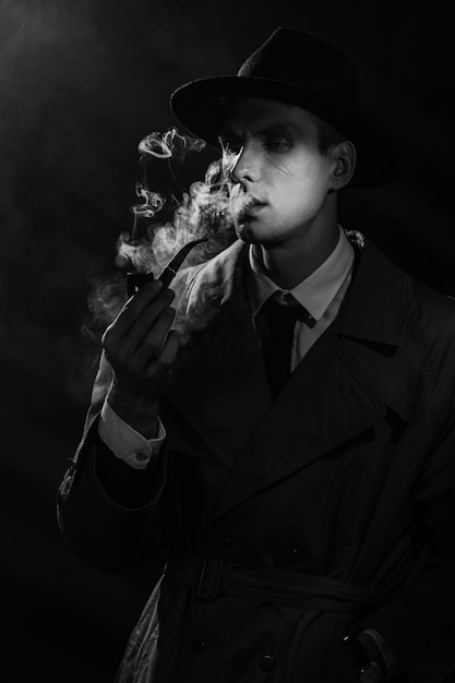 Foto ritratto noir scuro di un detective maschio che fuma una pipa retrò con tabacco concetto di indagine sulla spia del detective privato