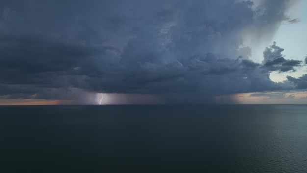 Dark ominous thunderstorm clouds forming on overcast sky during heavy rainfall season over ocean surface at sunset