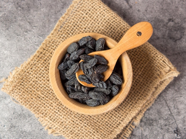 Dark raisins in a bowl on a dark concrete background